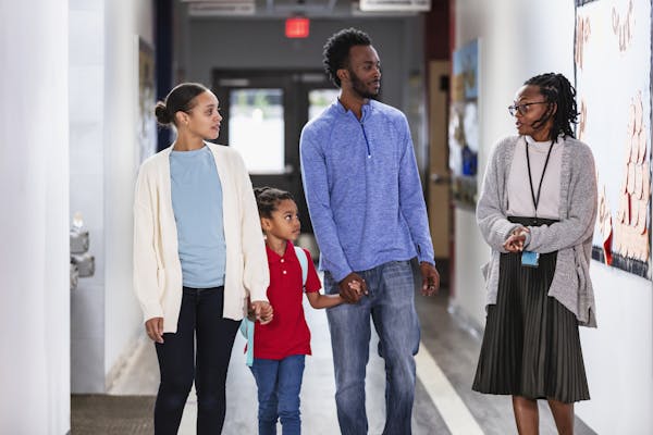 Two parents walk hand-in-hand in a school hallway while talking with an educator.