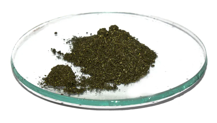 A glass dish holding a small mound of dark green crystalline powder