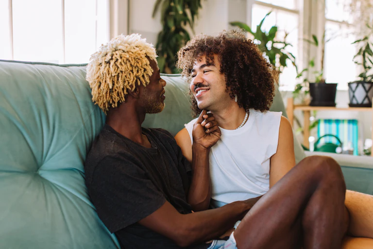two men sit on a couch together smiling at each other