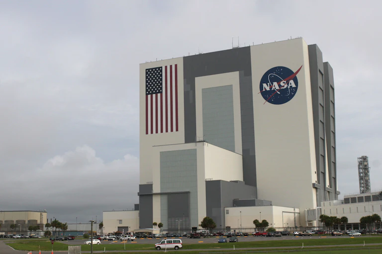 A tall building with an American flag and a NASA logo painted on its side, with storm clouds on the horizon.