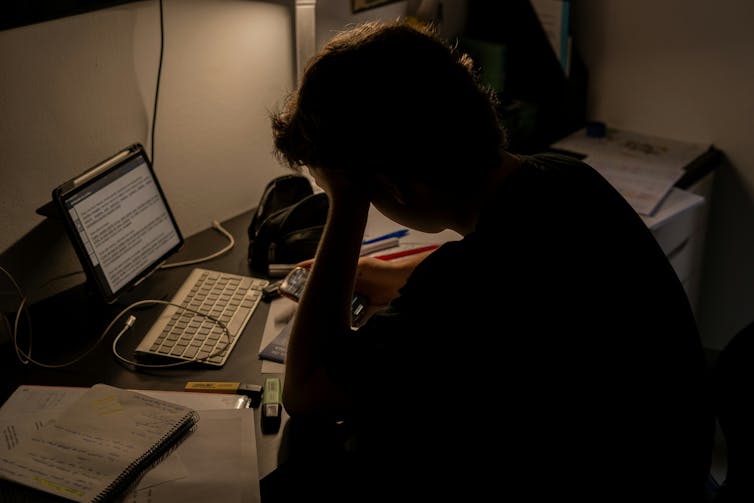 A person sits at a desk with their head in their hands