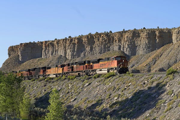 A train rolls along on a hillside with a flat bluff above it.