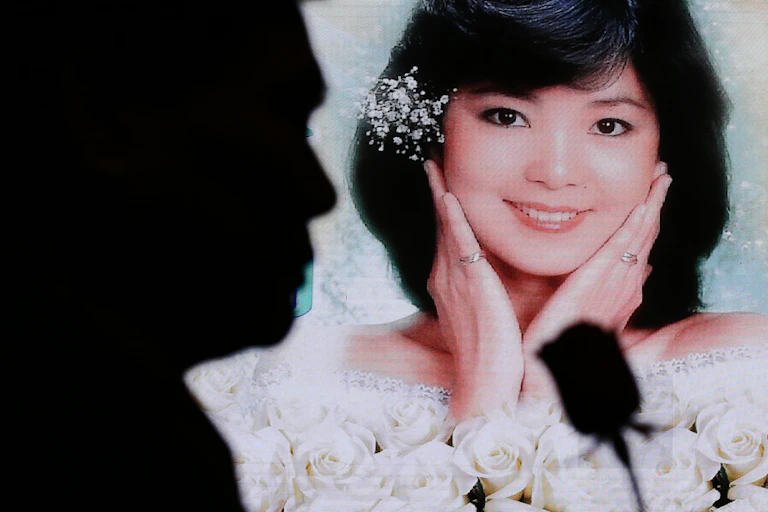Silhouette of a man holding a rose in front of a photograph of a smiling young woman surrounded by white roses.