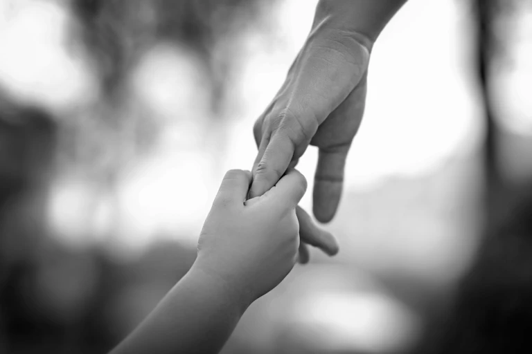 Two hands, fingers clasped, belonging to a child and a parent.