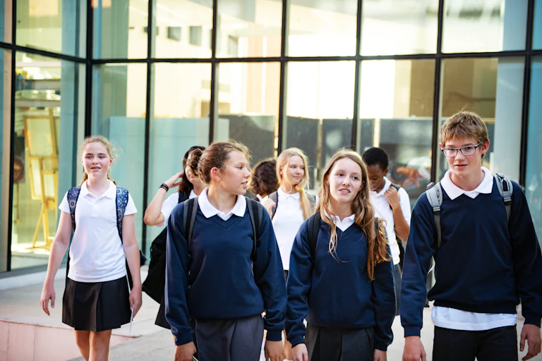 A group of high school students in uniform walk in an outdoor area.