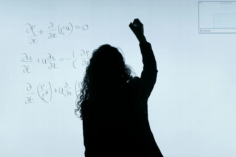 Silhouetted person with curly long hair writes on a backlit whiteboard.