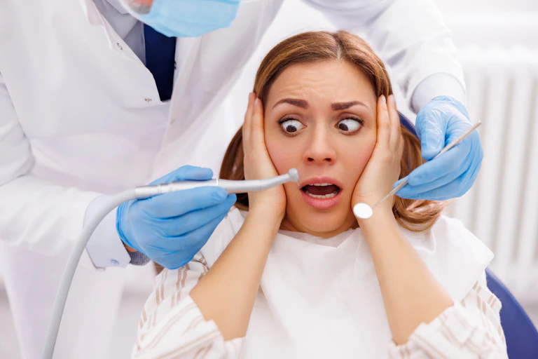 Woman afraid while sitting at dental chair at dentist office. Dentist is holding dental drill and angled mirror,