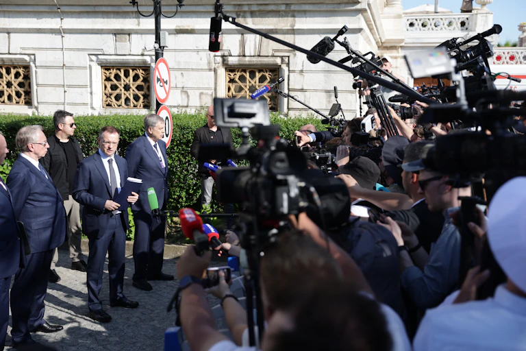 A group of men in suits with a large media contingent.