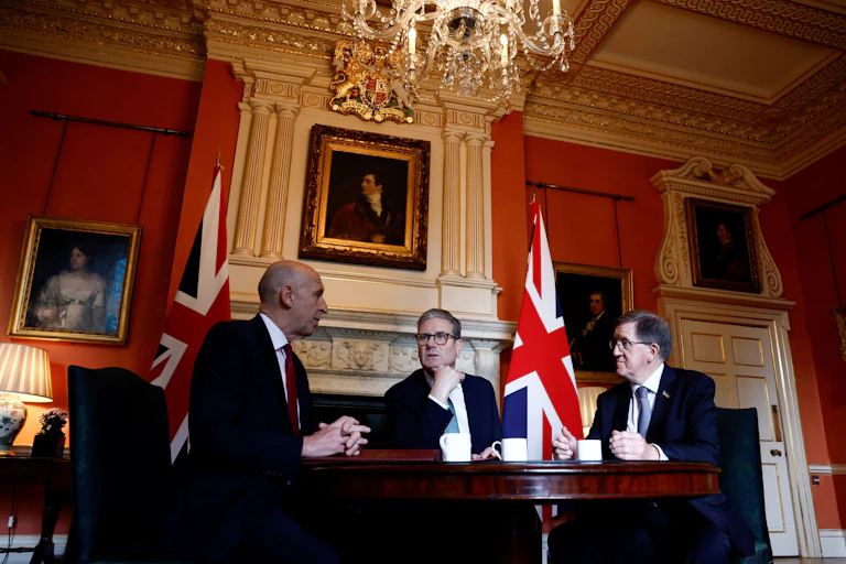 Healey, Starmer and Robertson sitting and talking around a table in a grand, red-walled room.