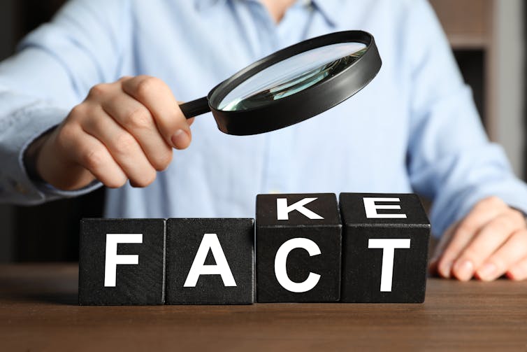 A person hold a magnifying glass over block letters that spell out the word fact.