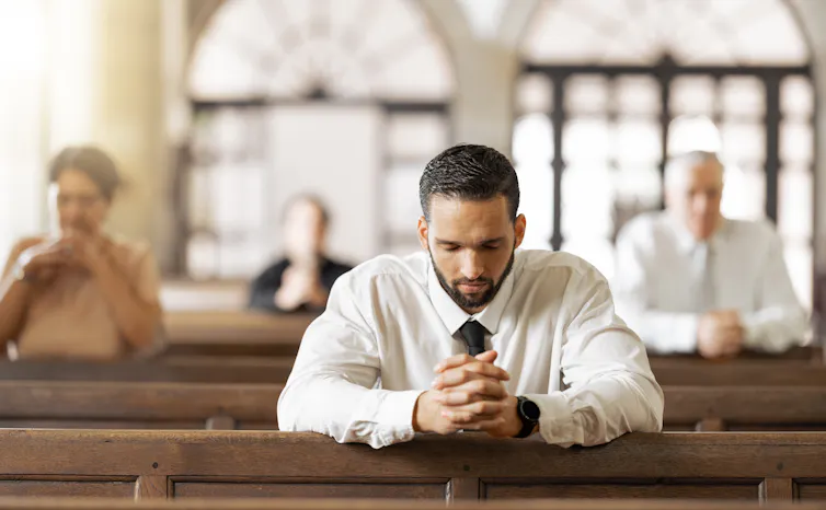 Stock photo of a young man kneeling and bowing his head in prayer in a church pew