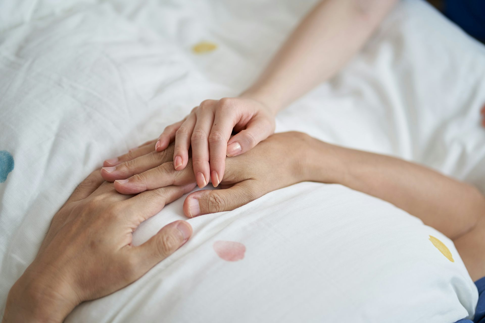 Des mains se touchent sur un lit.