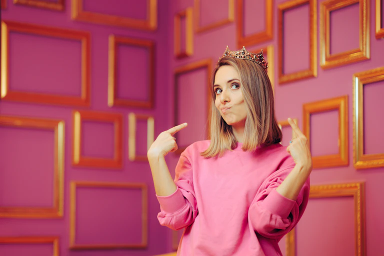 Woman wearing a crown and pointing to herself.