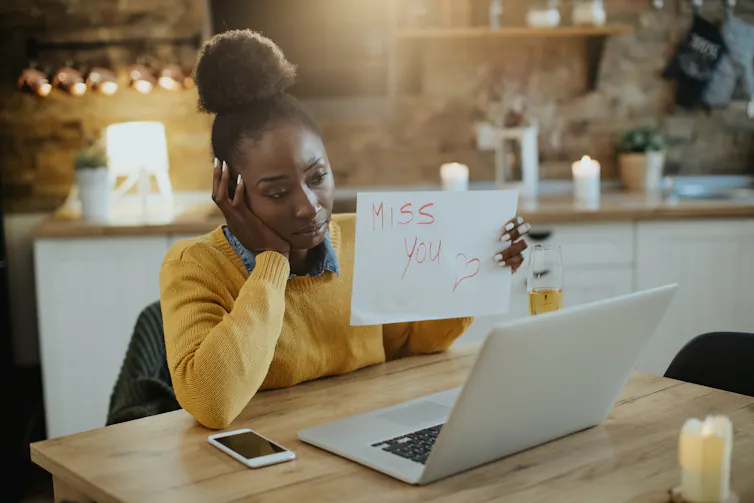 Woman sad holding up a piece of paper that says 'I miss you' so it can be seen through her webcam.