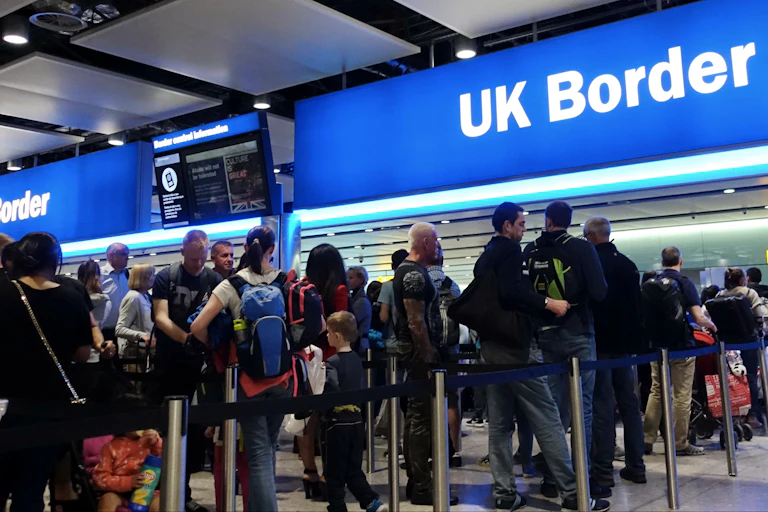 travellers queuing to come through a UK immigration desk