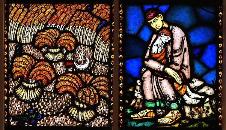A stained glass window depicting an image of a man seated on the ground and cradling a child in his lap.