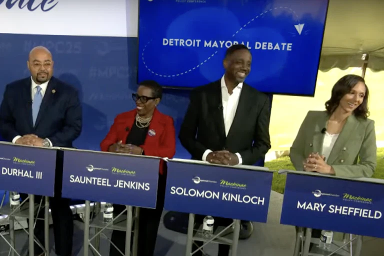 Three men and two women stand behind blue lecterns in business attire