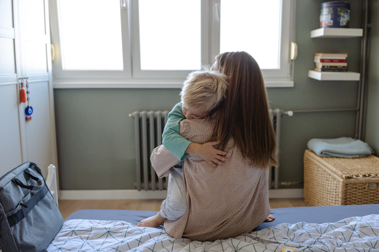 The back of a mother sitting on her bed hugging her child