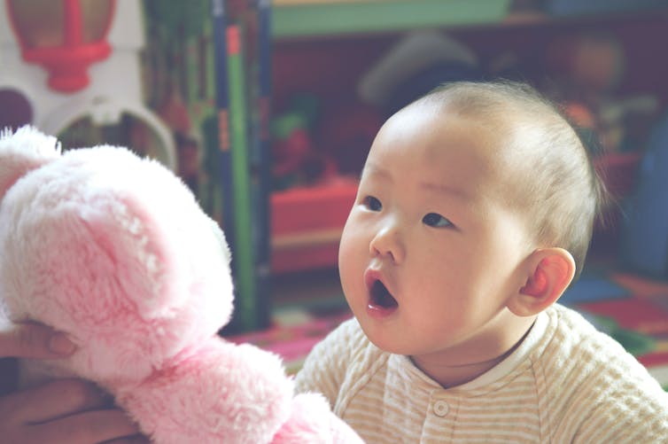 a baby speaks to a pink stuffed toy