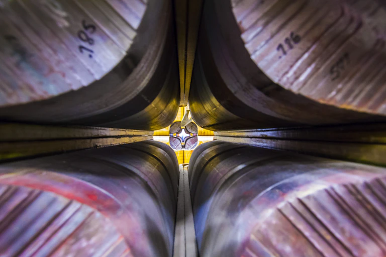 A symmetric, cross-shaped view of the gap between four long rows of magnets ending in a complex, brightly lit device.