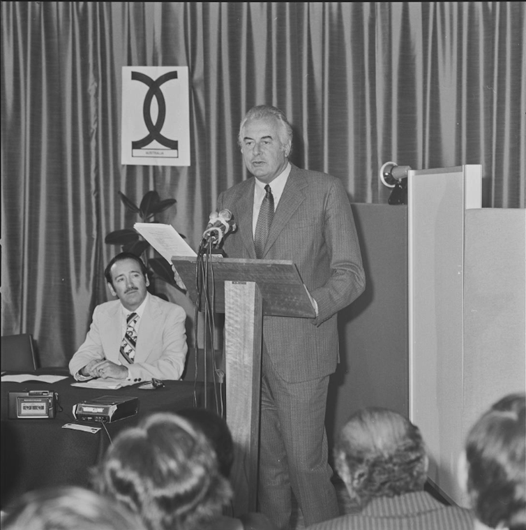 Gough Whitlam stands at a lectern and speaks to a crowd.