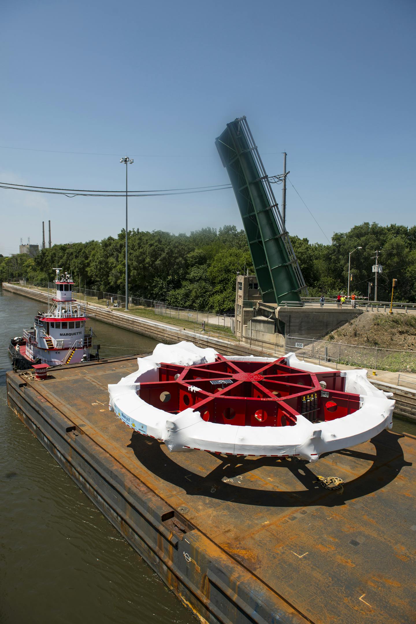 Photo of a large wheel-shaped device on a barge on a river.