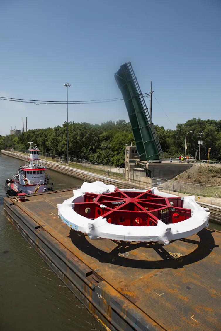 Photo of a large wheel-shaped device on a barge on a river.