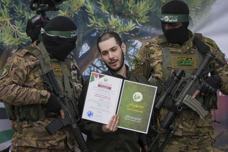 An Israeli hostage flanked on two sides by masked Hamas militants.