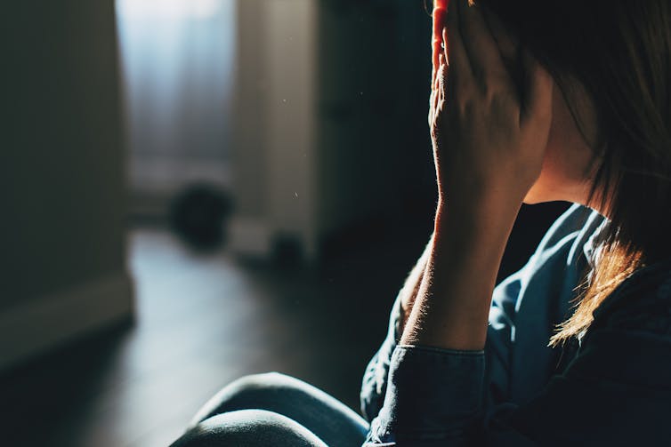 Person sitting against wall with knees pulled up, hands covering face