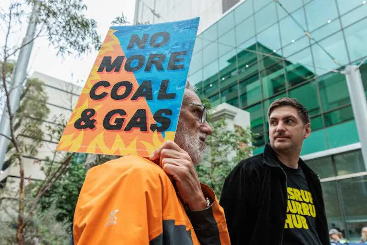 Two men, one holding a sign saying 'No more coal & gas'.