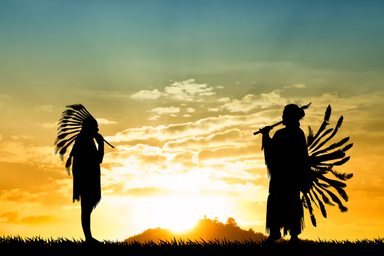 Two Native American Indians in traditional headdress set against a setting sun