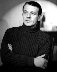 A black and white photo of a man in a polo neck jumper.