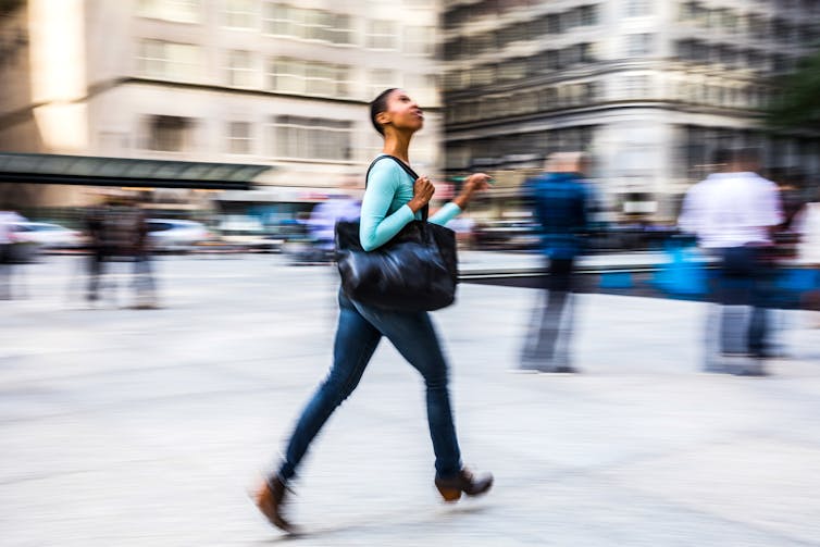 woman strides through city looking up, background is blurred around her