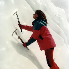 Alpinista segurando picaretas de gelo olhando para cima em uma montanha nevada.