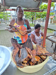 Deux femmes dans un marché, derrière une bassine remplie de morceaux de poisson fumé