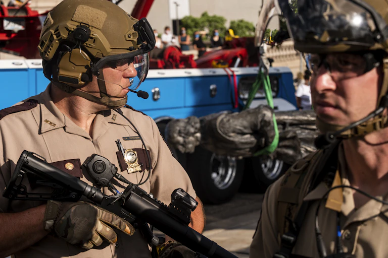 Two police officers holding rifles guard a toppled statue of Christopher Columbus.