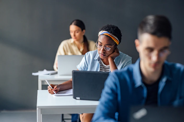 Three students sit at desks with laptops.