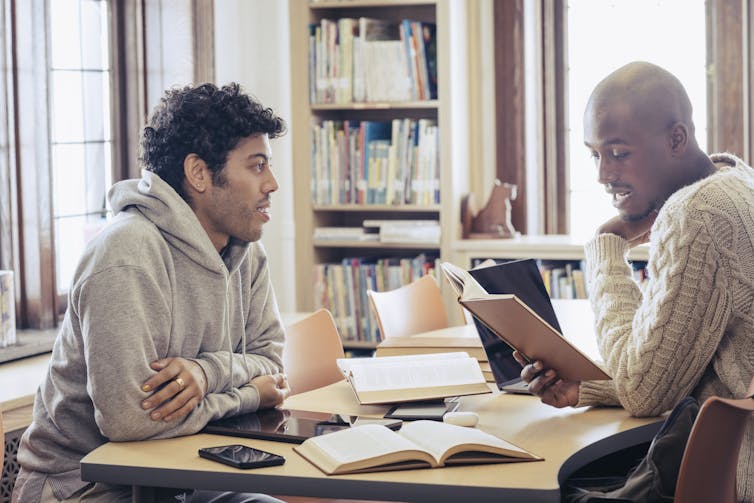 Two male students sit in a campus library reviewing notes.