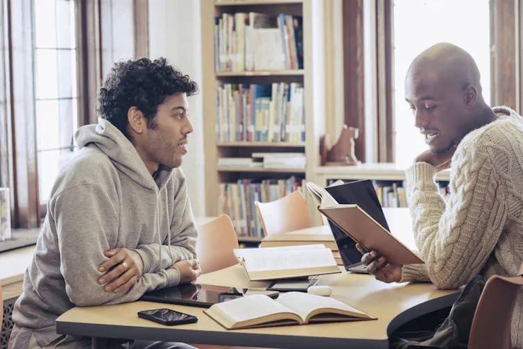 Two male students sit in a campus library reviewing notes.