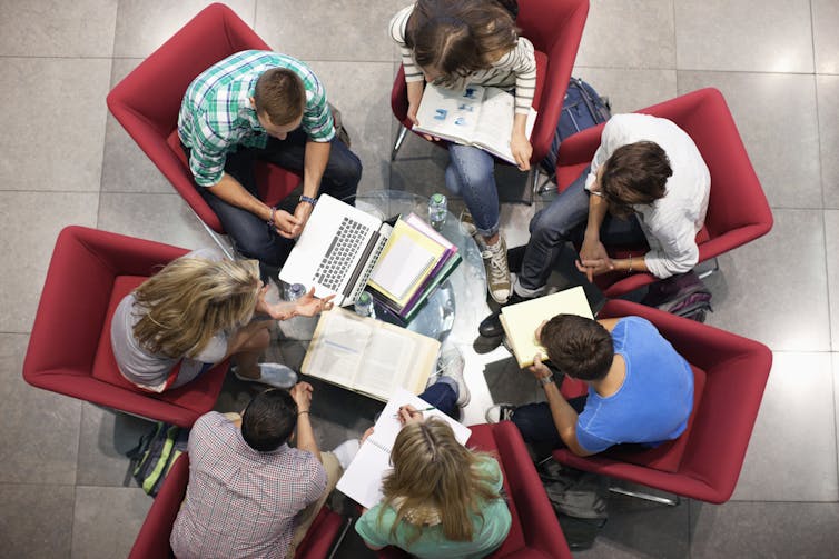 An overhead photo of students in a study group sitting around a small glass table.