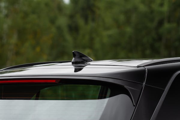 Top part of black car back showing shark finn antenna with trees in the background