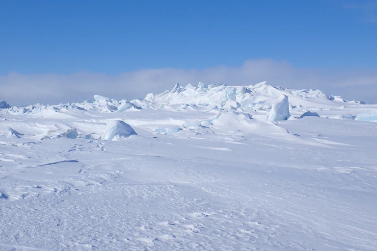 A white landscape with blocky ridges extends under a blue sky.