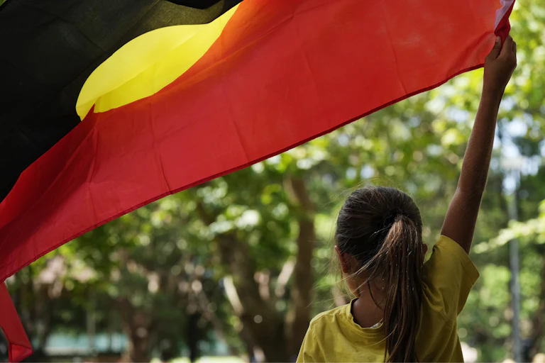 Young girl waving a large Aboriginal flag.