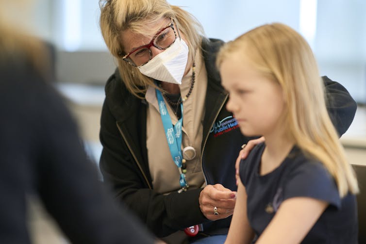 La mujer que lleva una máscara le da inyección a una niña