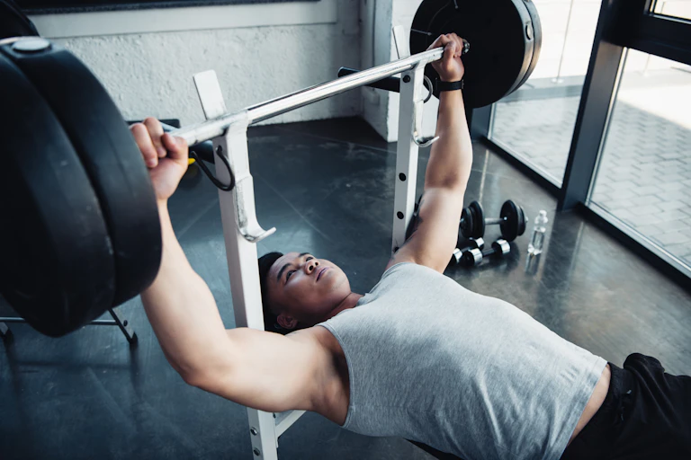A young man performs a bench press with a barbell.