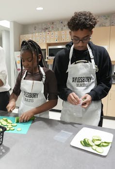 La crisis de accesibilidad de alimentos es una de las razones por las que los gobiernos necesitan para reforzar la comida escolar 2 Los jóvenes que usan delantales cortan pepinos en la cocina.