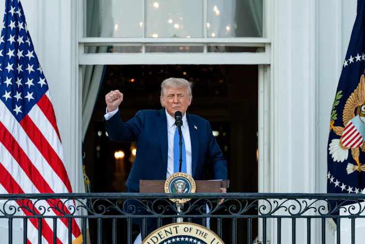 Donald Trump stands on the White House balcony and makes a ckenched fist gesture.