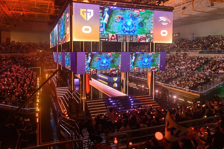 Hundreds of seated people watch a giant screen.