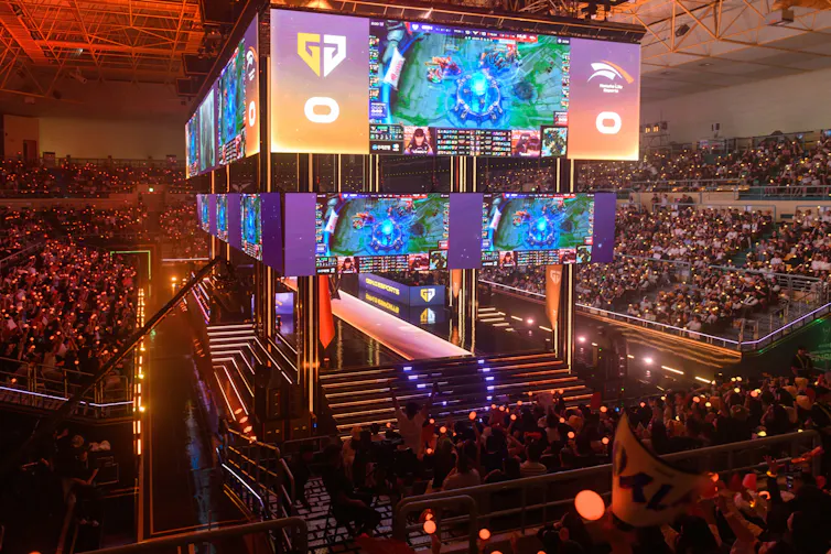 Hundreds of seated people watch a giant screen.