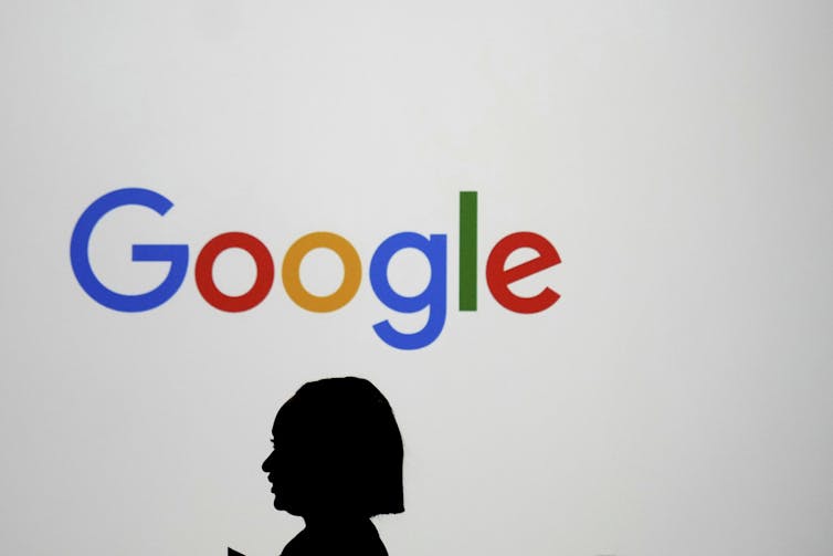 a woman's head is silhouetted against a large screen displaying the Google logo